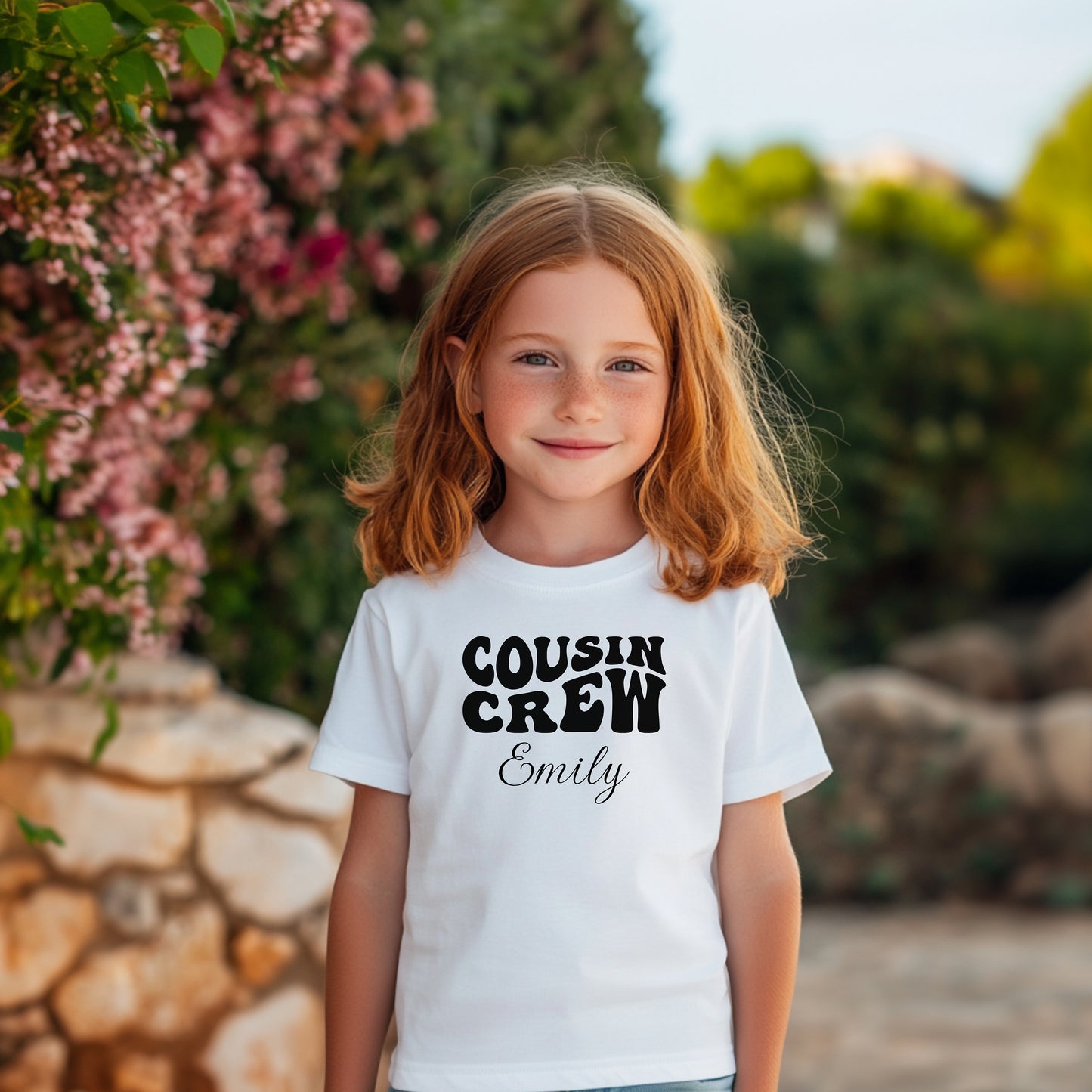Smiling toddler wearing a White T-shirt featuring a bold black "Cousin Crew" design with “Your Name” in a cursive font underneath. The shirt has a casual fit and is styled with denim jeans, creating a playful and adorable look perfect for family events or matching cousin outfits.