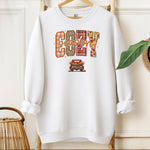White Gildan sweatshirt featuring a colorful “Cozy Season” design with bold patterned letters—plaid, leopard, gingham, and fall leaves—and a retro red truck filled with pumpkins and sunflowers below. A festive and warm autumn look perfect for embracing pumpkin spice vibes, crisp air, and cozy fall days.