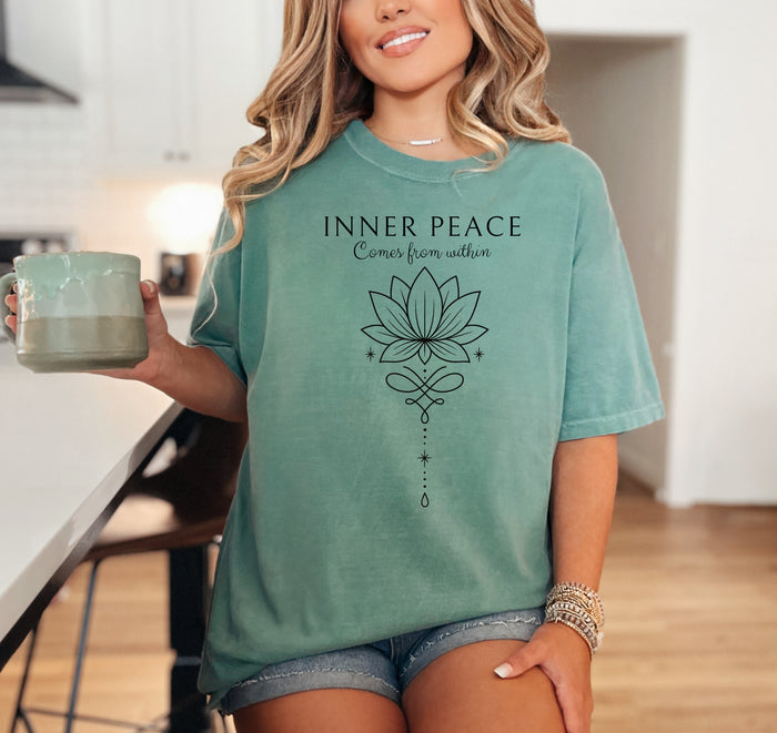 Person wearing a light green T-shirt featuring an “Inner Peace Comes from Within” design with a black line art lotus flower and elegant ornamental accents. The minimalist, symmetrical artwork conveys tranquility, mindfulness, and spiritual balance, making it perfect for yoga enthusiasts, meditation lovers, and those seeking calm, positive energy in their everyday style.