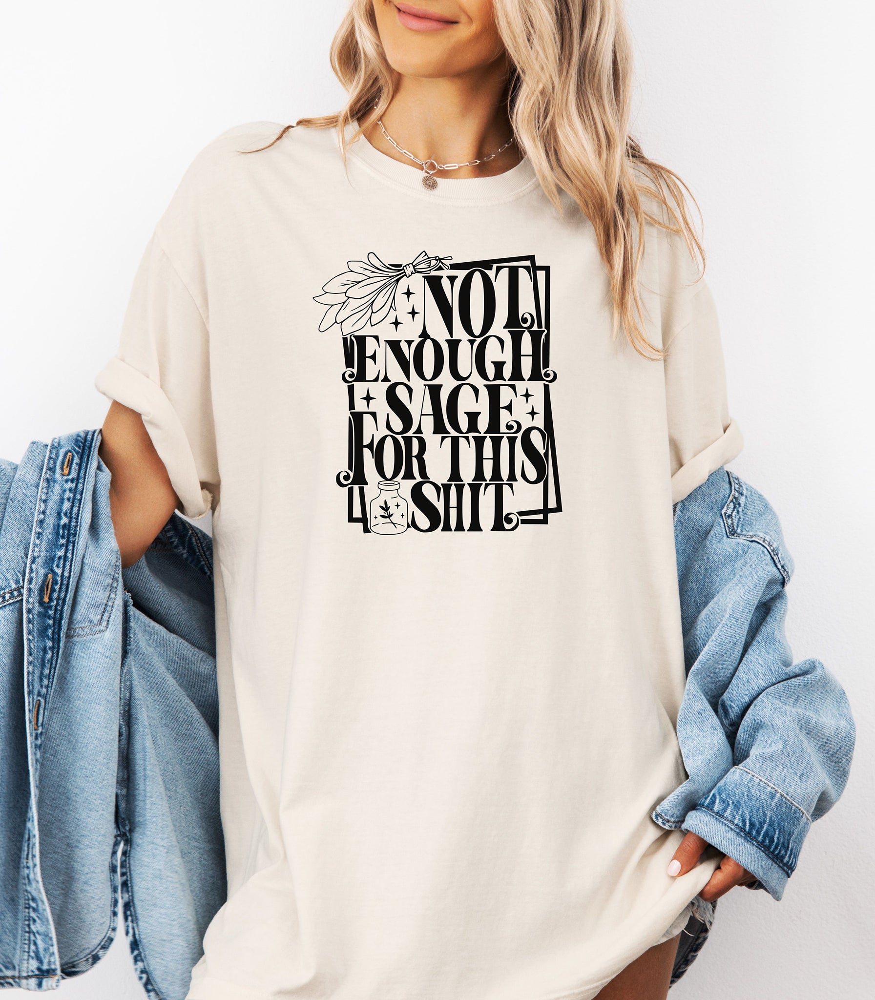 Ivory T-shirt with bold black typography reading “Not Enough Sage For This Shit,” accented with illustrated sage leaves, sparkles, and a small potion jar with a leafy design. Playful and cheeky statement shirt for spiritual, witchy, or humor-loving personalities.