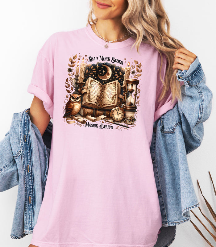 Person wearing a blossom pink t-shirt featuring a whimsical "Read More Books, Magick Awaits" design. The graphic showcases an open enchanted book surrounded by candles, a crescent moon, owl, pocket watch, hourglass, and magical elements, creating a mystical and literary aesthetic perfect for book lovers and fantasy fans.