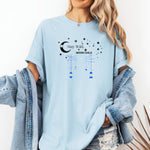Stay Wild Moon Child T-shirt featuring a celestial design with a crescent moon, stars, and hanging lanterns. The text 'Stay Wild, Moon Child' is surrounded by cosmic elements, evoking a dreamy bohemian vibe. Printed on a chambray light blue unisex tee, this mystical and free-spirited graphic is perfect for astrology lovers, night sky dreamers, and those who embrace their wild, cosmic side.