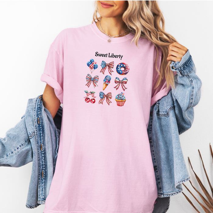 Blossom pink t-shirt featuring a festive 'Sweet Liberty' design with patriotic icons including bows, cherries, a donut, ice cream cone, and cupcake decorated in red, white, and blue stars and stripes. Fun, colorful 4th of July and summer celebration shirt perfect for parties, barbecues, and casual wear.