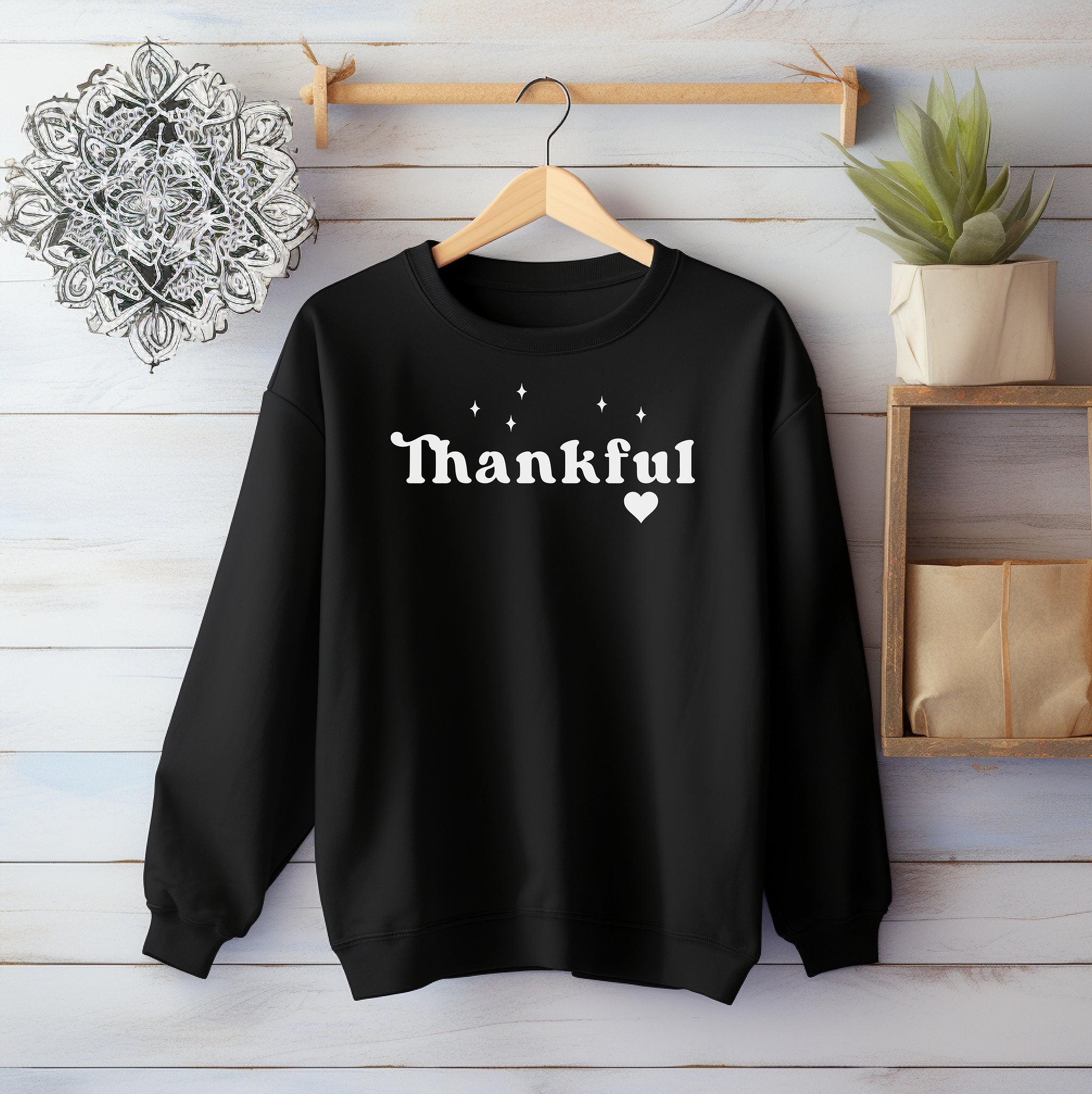 Black Gildan sweatshirt featuring the word “Thankful” in bold white retro-style font, accented with small sparkling stars above and a heart below. A simple yet meaningful design that celebrates gratitude and cozy fall vibes—perfect for Thanksgiving, autumn gatherings, or everyday wear.