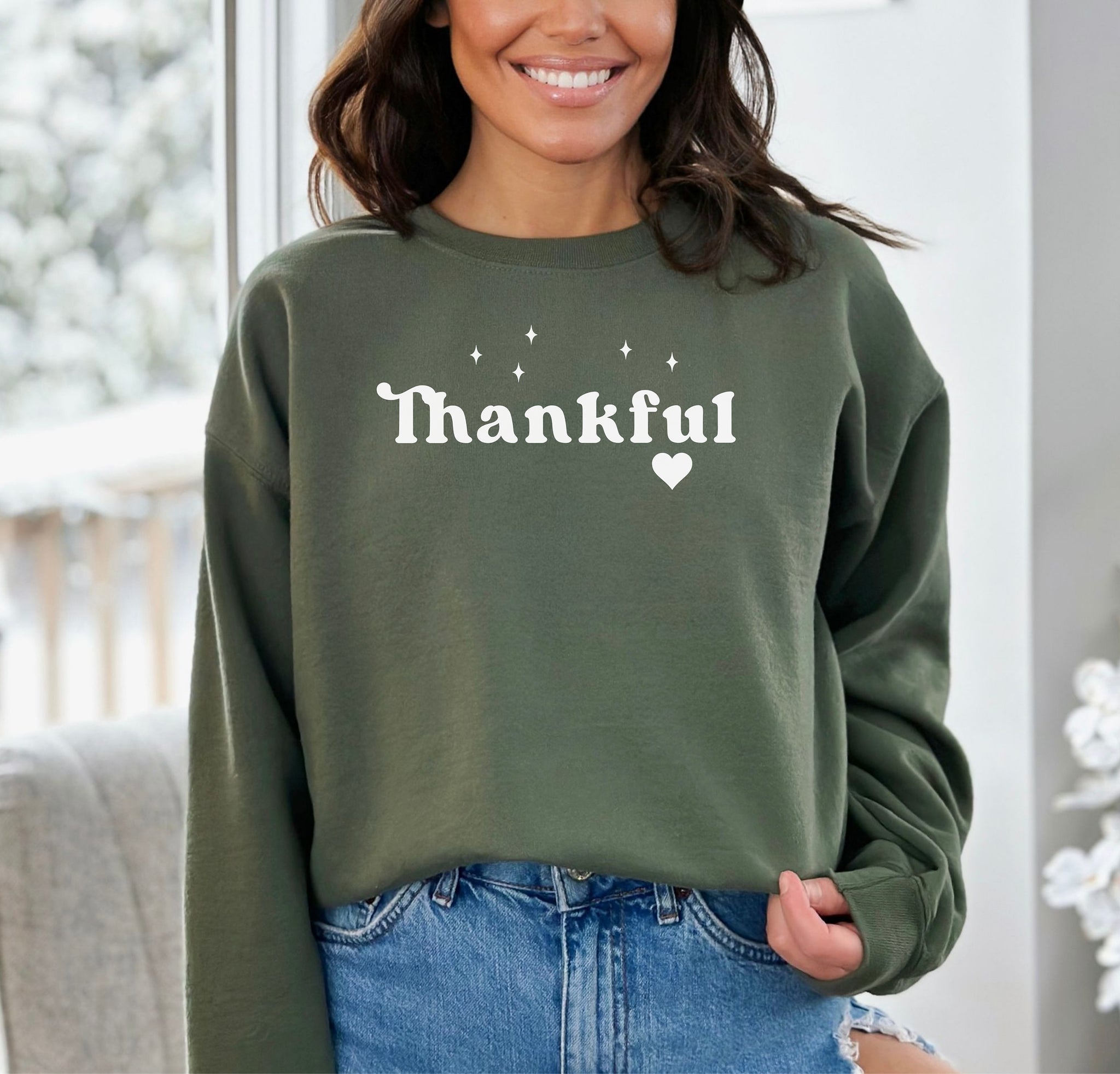Military Green Gildan sweatshirt featuring the word “Thankful” in bold white retro-style font, accented with small sparkling stars above and a heart below. A simple yet meaningful design that celebrates gratitude and cozy fall vibes—perfect for Thanksgiving, autumn gatherings, or everyday wear.