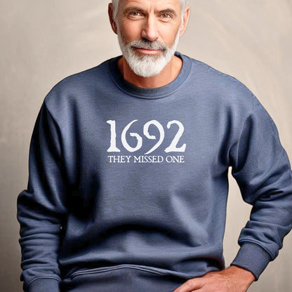 Man wearing a Heather Sport Dark Navy sweatshirt with '1692 THEY MISSED ONE' text on a beige background