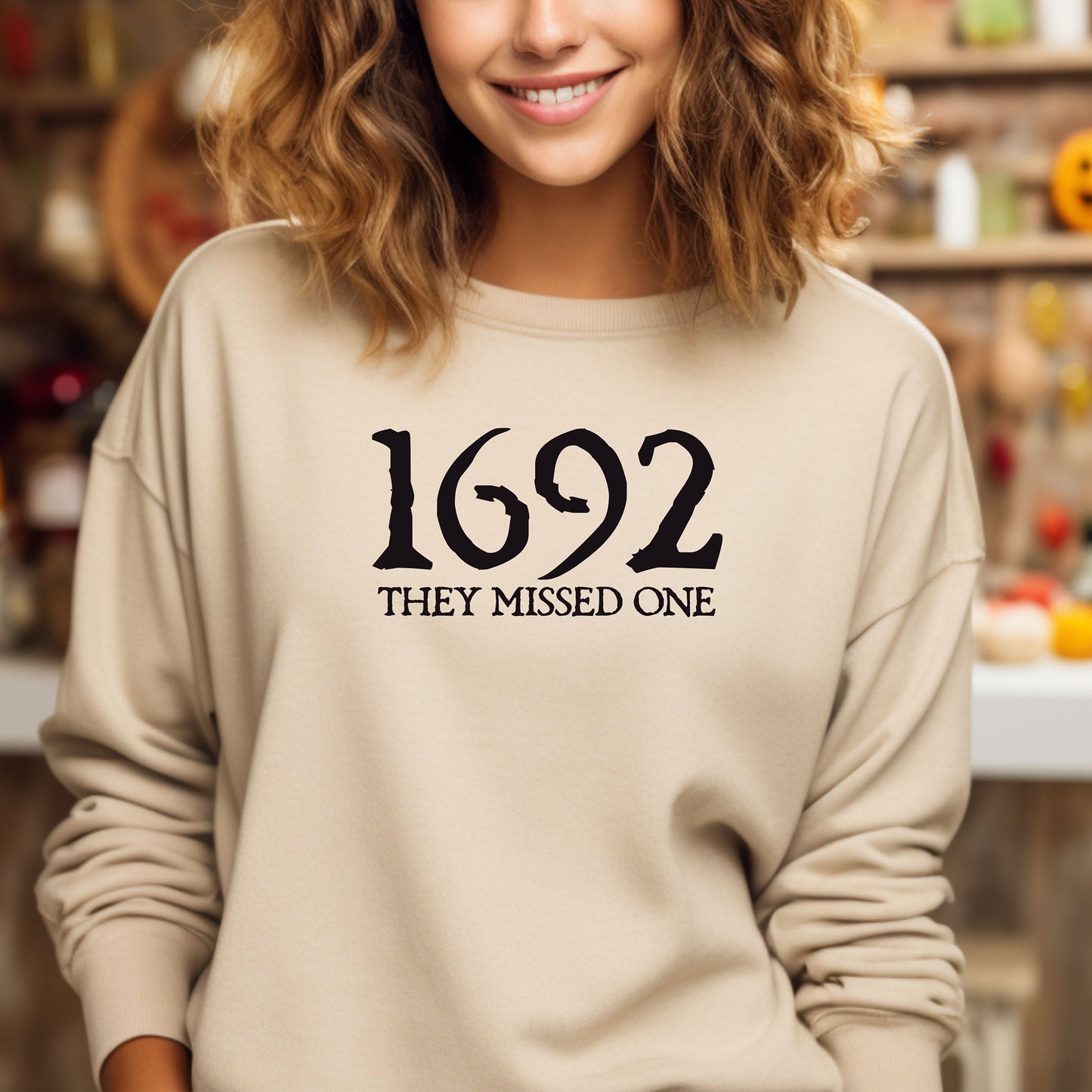 Person wearing a sand sweatshirt with '1692 THEY MISSED ONE' text in a casual fall setting.