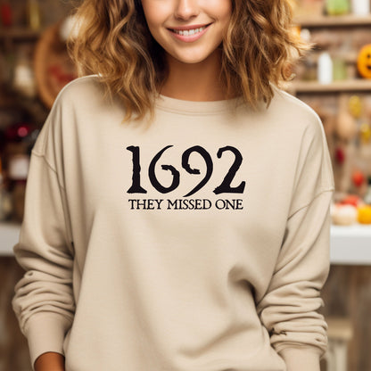 Person wearing a sand sweatshirt with '1692 THEY MISSED ONE' text in a casual fall setting.
