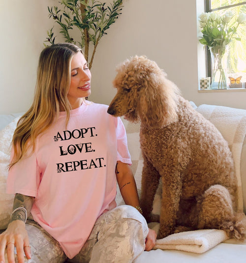 Adopt. Love. Repeat. T-shirt featuring bold black text with small puppy and kitten accents incorporated into the letters. Printed on a soft, blossom pink unisex tee, this design is perfect for pet lovers, rescue advocates, and animal adoption supporters. Ideal for wearing to adoption events, volunteering at shelters, or showing pride in giving animals a forever home.
