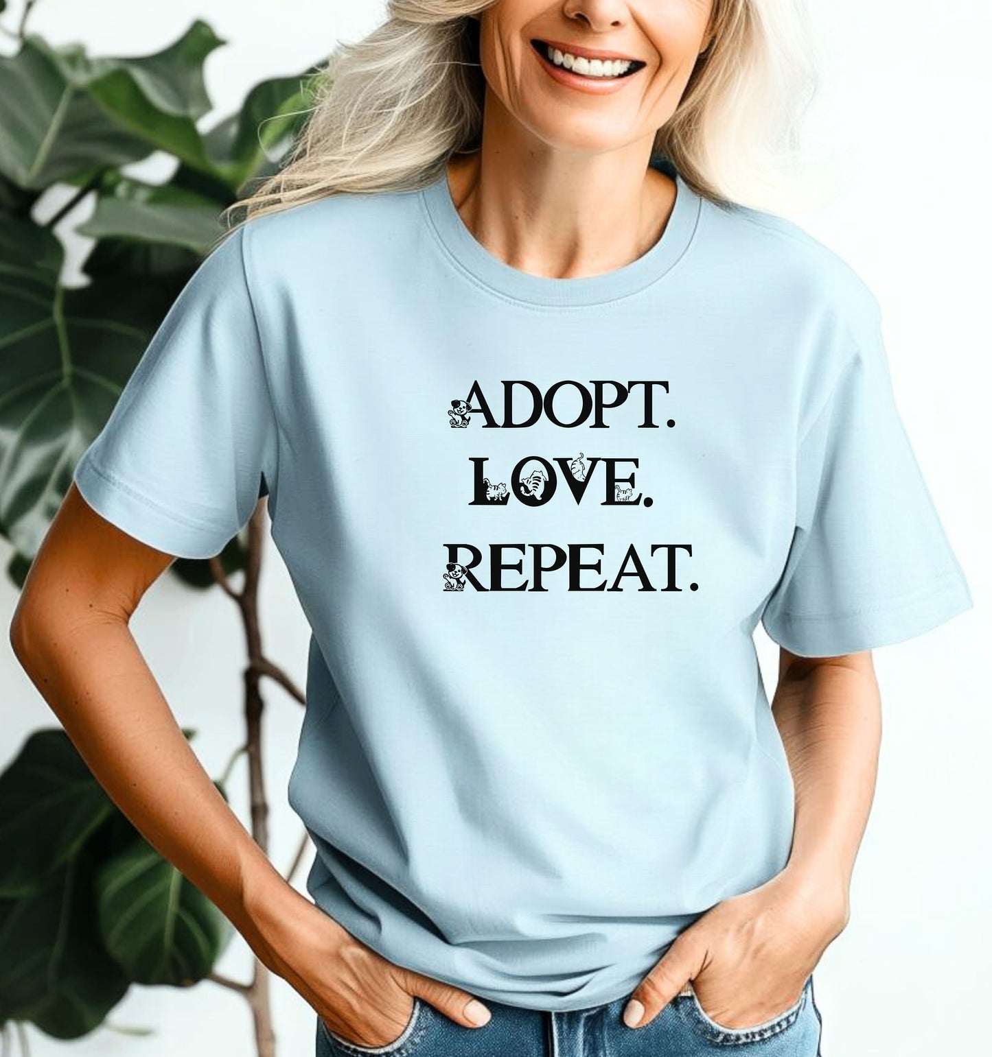 Adopt. Love. Repeat. T-shirt featuring bold black text with small puppy and kitten accents incorporated into the letters. Printed on a soft, chambray light blue unisex tee, this design is perfect for pet lovers, rescue advocates, and animal adoption supporters. Ideal for wearing to adoption events, volunteering at shelters, or showing pride in giving animals a forever home.