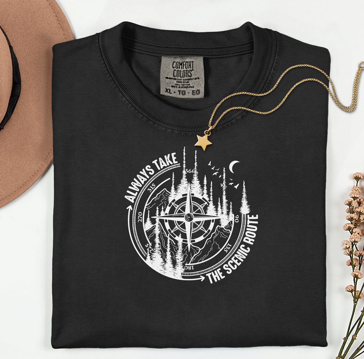 Always Take The Scenic Route T-shirt featuring a detailed compass design surrounded by tall pine trees, mountains, a crescent moon, and flying birds. This outdoor adventure graphic symbolizes exploration, travel, and a love for nature. Printed on a soft, comfortable black unisex tee, it’s perfect for hikers, campers, and wanderers who embrace the beauty of the journey and prefer the scenic path over the fast route.