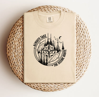 Always Take The Scenic Route T-shirt featuring a detailed compass design surrounded by tall pine trees, mountains, a crescent moon, and flying birds. This outdoor adventure graphic symbolizes exploration, travel, and a love for nature. Printed on a soft, comfortable ivory unisex tee, it’s perfect for hikers, campers, and wanderers who embrace the beauty of the journey and prefer the scenic path over the fast route.