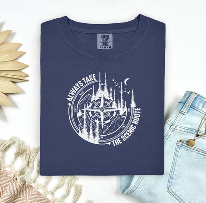 Always Take The Scenic Route T-shirt featuring a detailed compass design surrounded by tall pine trees, mountains, a crescent moon, and flying birds. This outdoor adventure graphic symbolizes exploration, travel, and a love for nature. Printed on a soft, comfortable navy unisex tee, it’s perfect for hikers, campers, and wanderers who embrace the beauty of the journey and prefer the scenic path over the fast route.