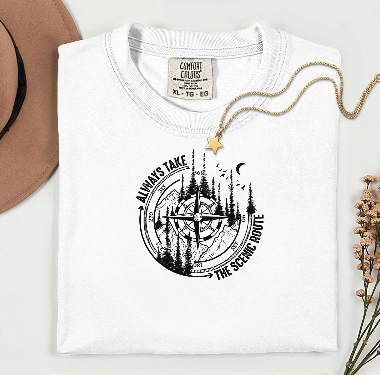 Always Take The Scenic Route T-shirt featuring a detailed compass design surrounded by tall pine trees, mountains, a crescent moon, and flying birds. This outdoor adventure graphic symbolizes exploration, travel, and a love for nature. Printed on a soft, comfortable white unisex tee, it’s perfect for hikers, campers, and wanderers who embrace the beauty of the journey and prefer the scenic path over the fast route.