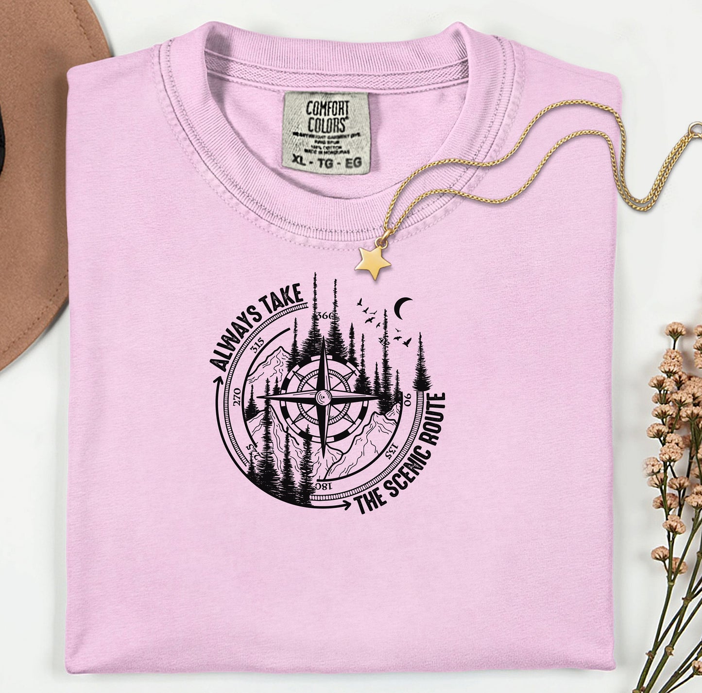 Always Take The Scenic Route T-shirt featuring a detailed compass design surrounded by tall pine trees, mountains, a crescent moon, and flying birds. This outdoor adventure graphic symbolizes exploration, travel, and a love for nature. Printed on a soft, comfortable blossom pink unisex tee, it’s perfect for hikers, campers, and wanderers who embrace the beauty of the journey and prefer the scenic path over the fast route.