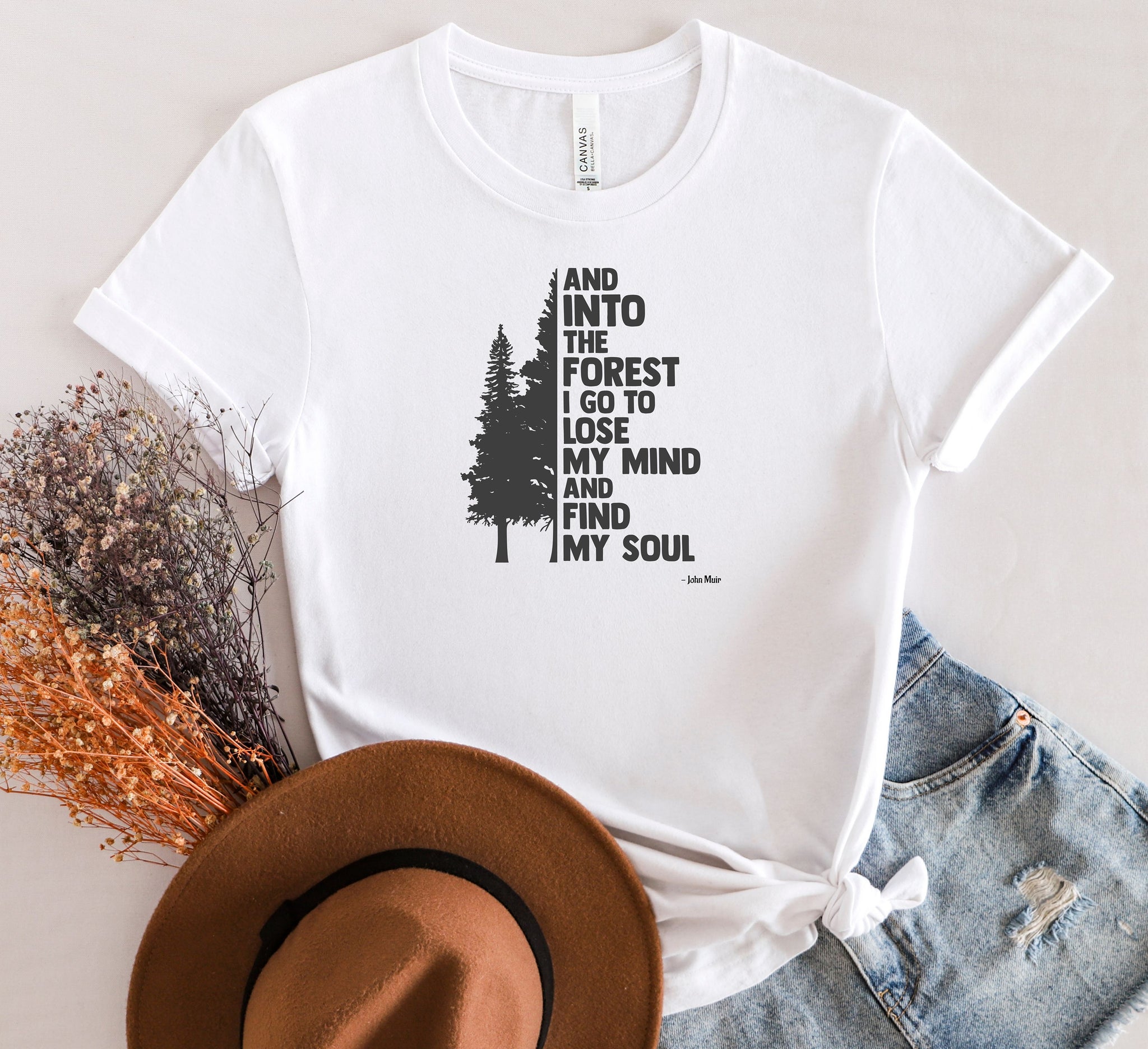 And Into The Forest I Go To Lose My Mind And Find My Soul T-shirt featuring a minimalist nature-inspired design with a tall pine tree alongside bold text of the famous John Muir quote. Printed on a soft white unisex tee, this design celebrates mindfulness, outdoor adventure, and the healing power of nature. Perfect for hikers, campers, and forest lovers who find peace and clarity in the wilderness.