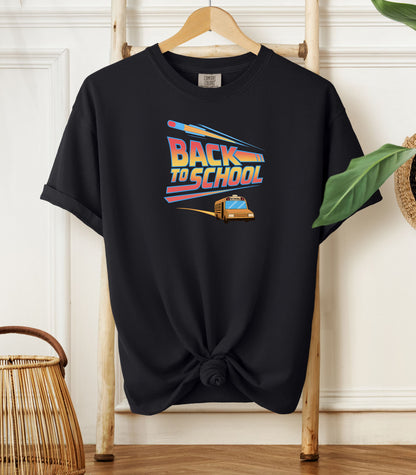 Person wearing a black t-shirt with a bold “Back to School” design featuring retro-style typography, a large pencil graphic above the text, and a yellow school bus driving below. A fun and colorful tee perfect for celebrating the new school year with energy and excitement.