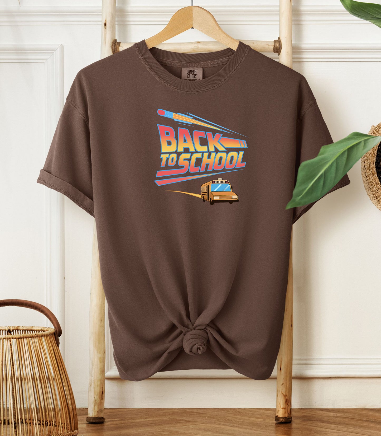 Person wearing an espresso t-shirt with a bold “Back to School” design featuring retro-style typography, a large pencil graphic above the text, and a yellow school bus driving below. A fun and colorful tee perfect for celebrating the new school year with energy and excitement.