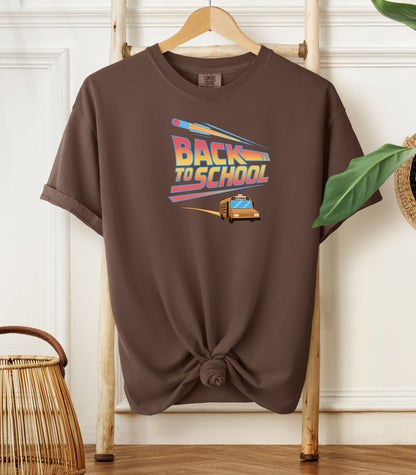Person wearing an espresso t-shirt with a bold “Back to School” design featuring retro-style typography, a large pencil graphic above the text, and a yellow school bus driving below. A fun and colorful tee perfect for celebrating the new school year with energy and excitement.