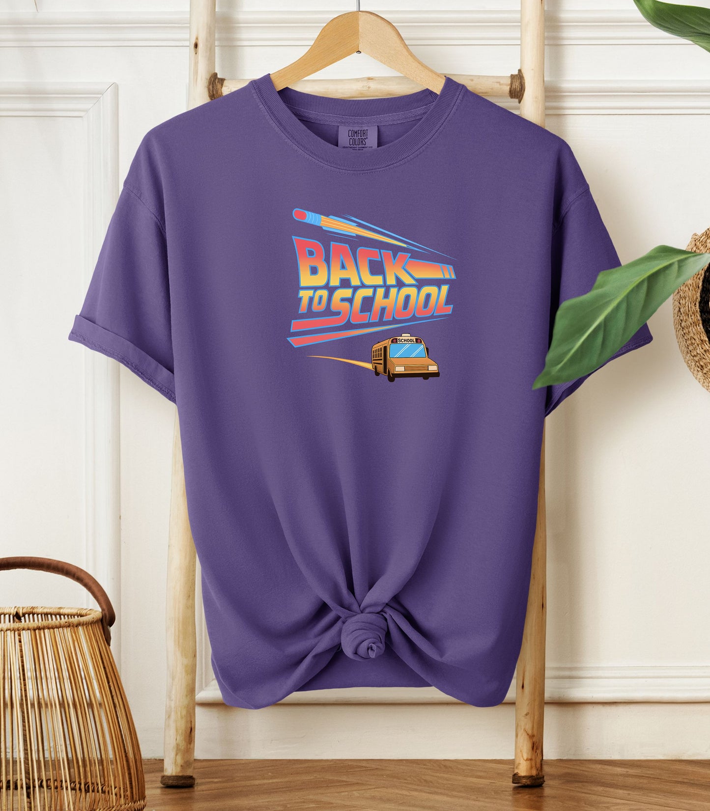 A grape t-shirt with a bold “Back to School” design featuring retro-style typography, a large pencil graphic above the text, and a yellow school bus driving below. A fun and colorful tee perfect for celebrating the new school year with energy and excitement.