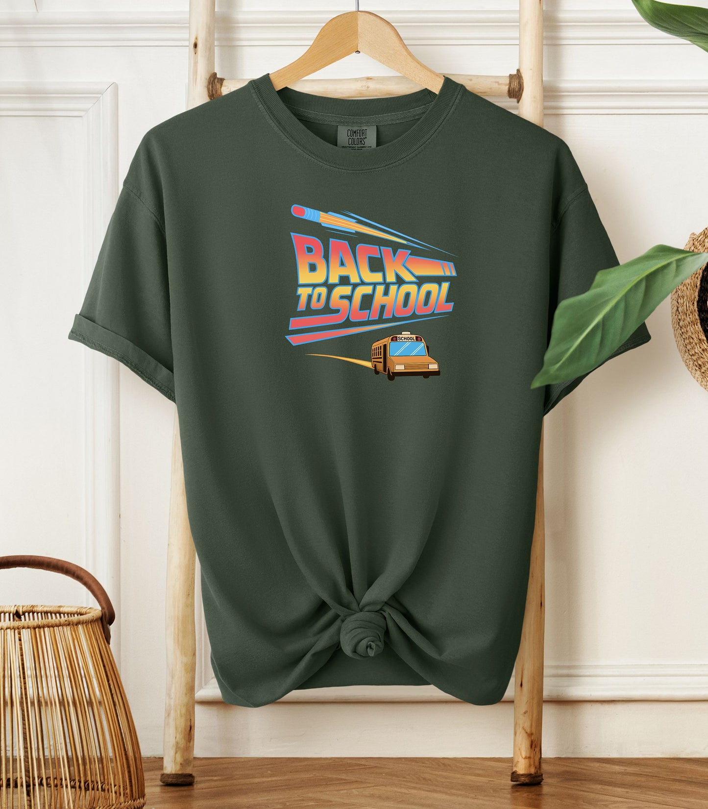 A Hemp color t-shirt with a bold “Back to School” design featuring retro-style typography, a large pencil graphic above the text, and a yellow school bus driving below. A fun and colorful tee perfect for celebrating the new school year with energy and excitement.