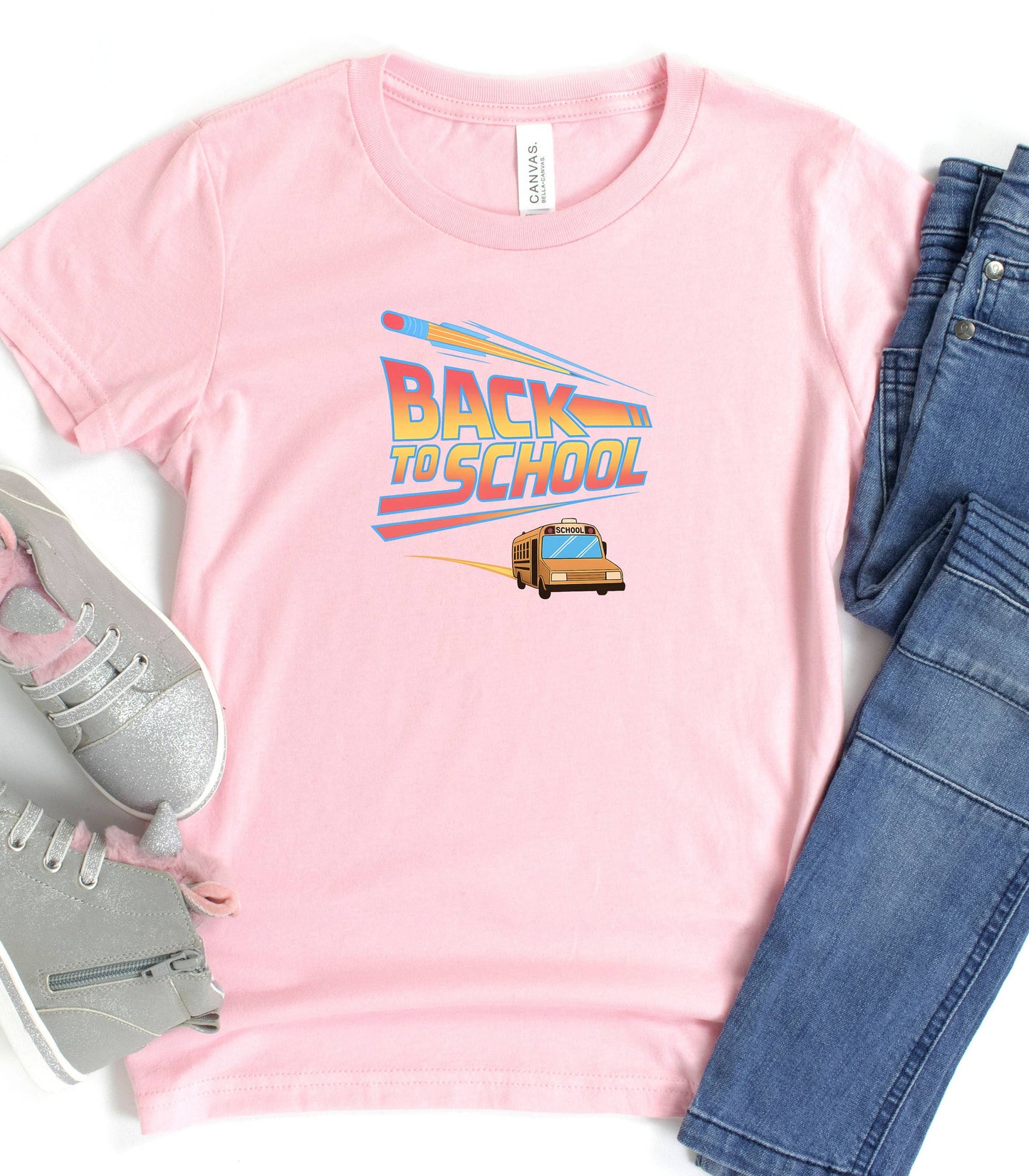 A pink t-shirt with a bold “Back to School” design featuring retro-style typography, a large pencil graphic above the text, and a yellow school bus driving below. A fun and colorful tee perfect for celebrating the new school year with energy and excitement.