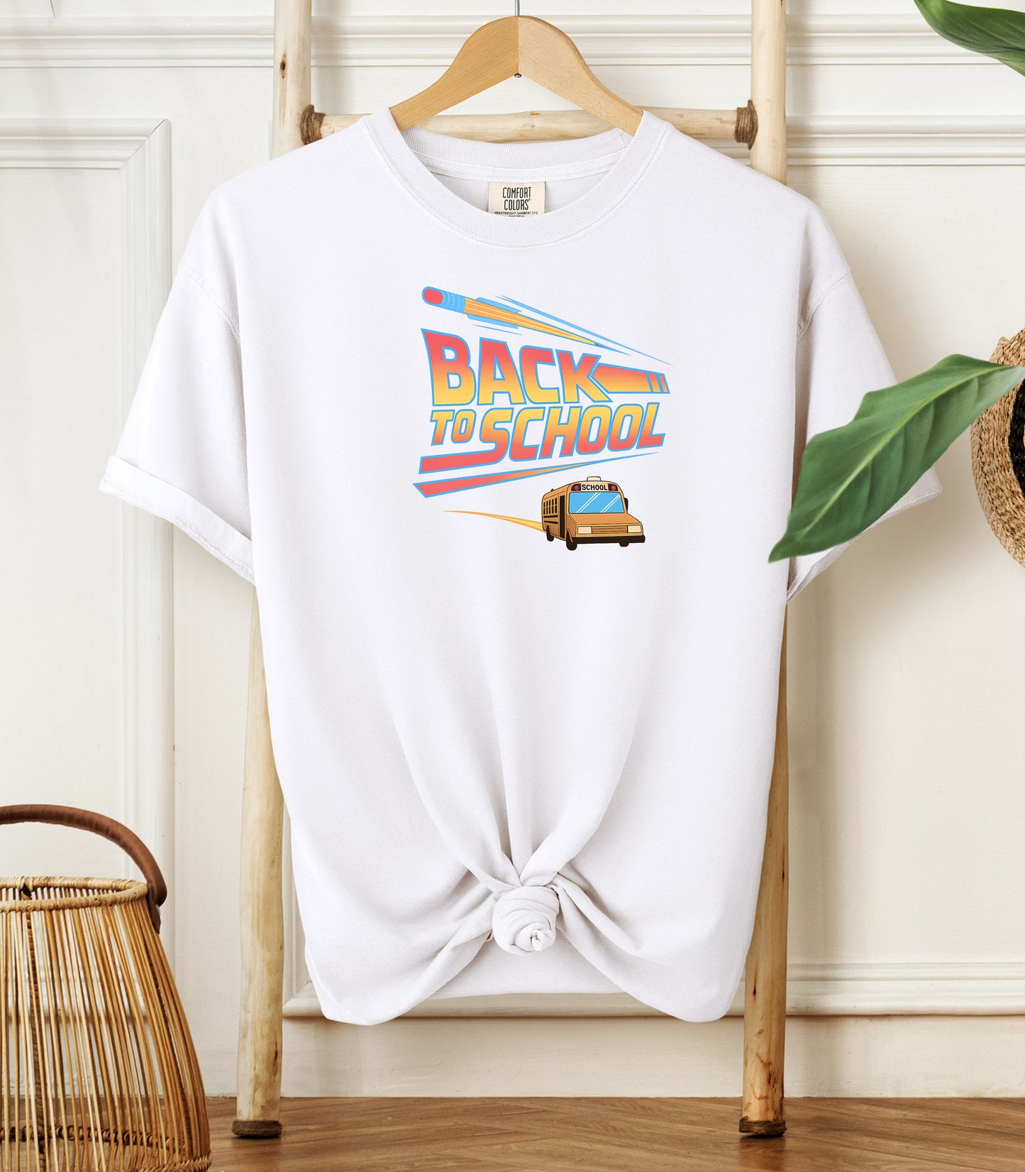 A White t-shirt with a bold “Back to School” design featuring retro-style typography, a large pencil graphic above the text, and a yellow school bus driving below. A fun and colorful tee perfect for celebrating the new school year with energy and excitement.