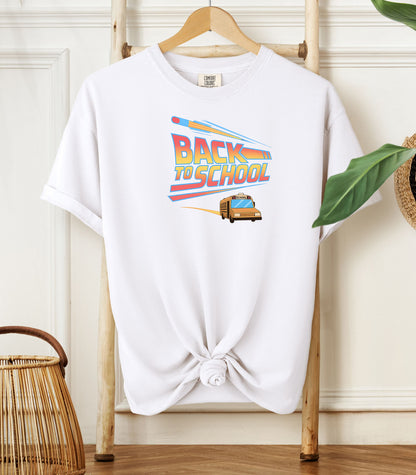A White t-shirt with a bold “Back to School” design featuring retro-style typography, a large pencil graphic above the text, and a yellow school bus driving below. A fun and colorful tee perfect for celebrating the new school year with energy and excitement.