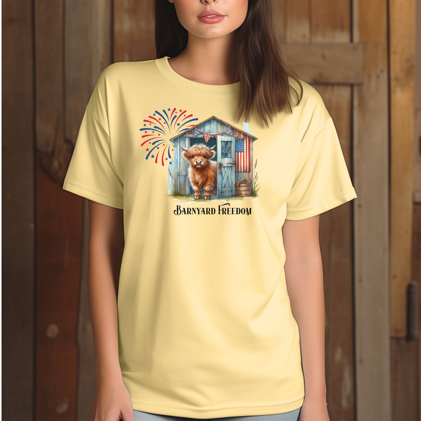 Banana t-shirt featuring a 'Barnyard Freedom' design with a cute Highland cow standing in front of a rustic blue barn decorated with an American flag. Red, white, and blue fireworks burst in the background, creating a festive patriotic country vibe. Perfect for 4th of July and farm life lovers.
