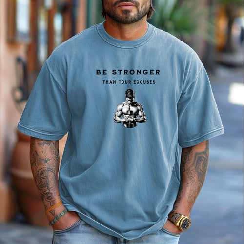 Person wearing a washed denim T-shirt featuring the motivational phrase “Be Stronger Than Your Excuses” in bold black lettering, with a graphic of a muscular figure holding a dumbbell below the text. Perfect for gym-goers, fitness enthusiasts, and athletes, this empowering workout shirt inspires determination, discipline, and strength training focus.