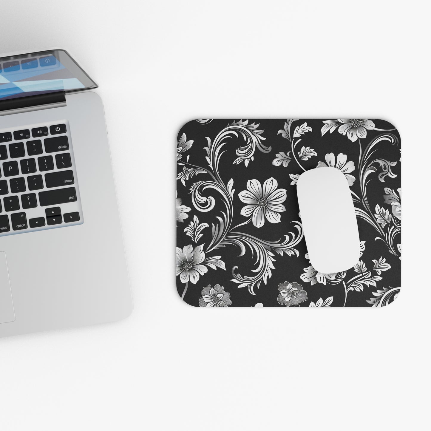 Floral black and white patterned mouse pad next to a laptop on a white background, with a white Apple mouse