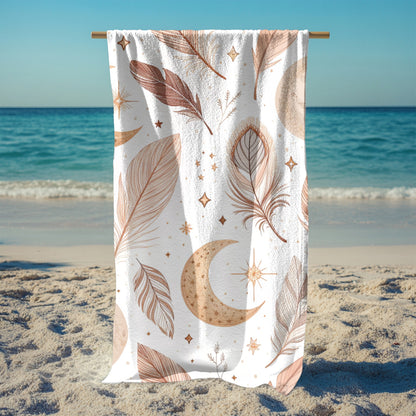 A white beach towel featuring a boho-style design with earthy-toned feathers, crescent moons, stars, and celestial accents hanging from a stand. Set against a sunny ocean backdrop, this mystical and artistic towel brings dreamy, free-spirited vibes—perfect for beach days, festivals, or mindful relaxation.
