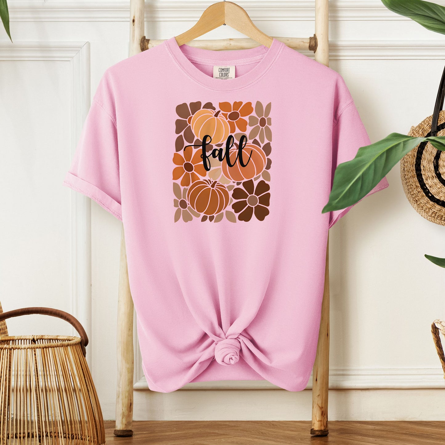 Blossom pink T-shirt featuring a boho-inspired fall design with hand-drawn pumpkins and flowers in warm autumn tones. The word "fall" is written in elegant script across the center of the graphic, framed by a mosaic-style floral and pumpkin pattern. Perfect for seasonal style and cozy autumn vibes.