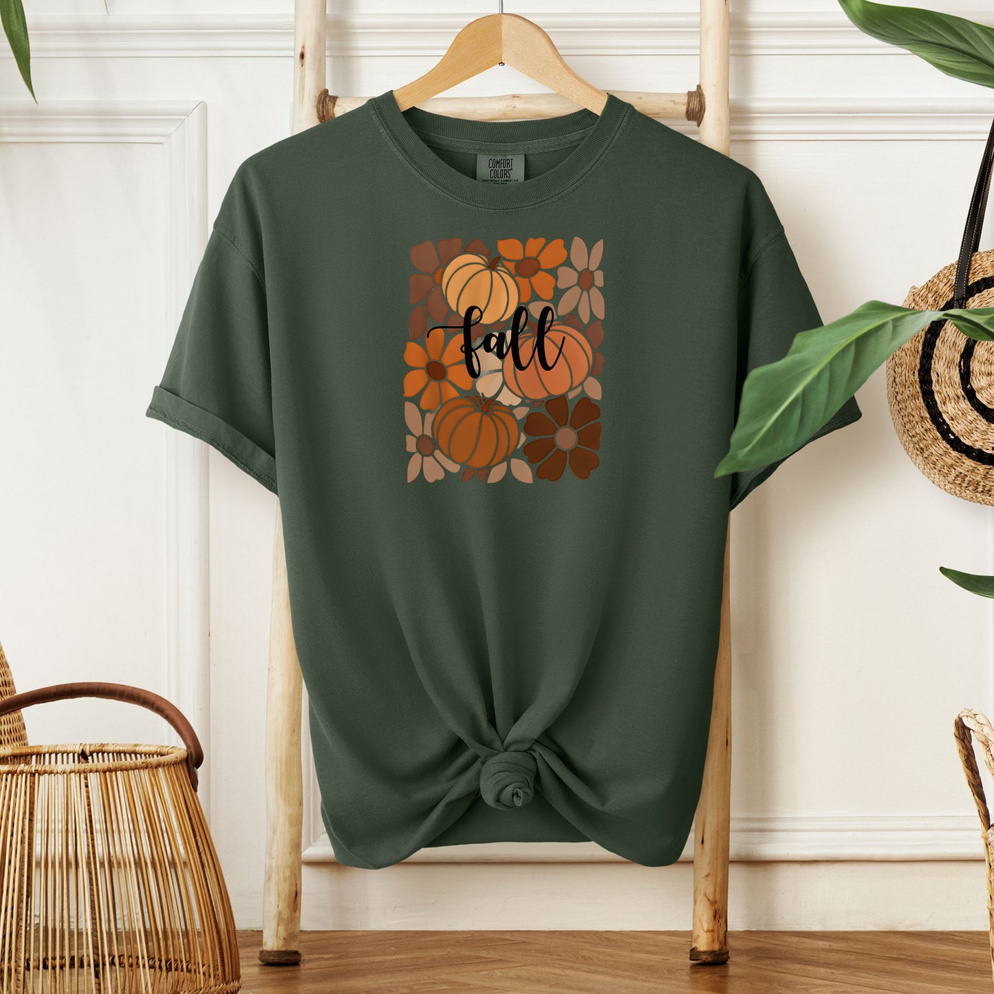 Hemp color T-shirt featuring a boho-inspired fall design with hand-drawn pumpkins and flowers in warm autumn tones. The word "fall" is written in elegant script across the center of the graphic, framed by a mosaic-style floral and pumpkin pattern. Perfect for seasonal style and cozy autumn vibes.