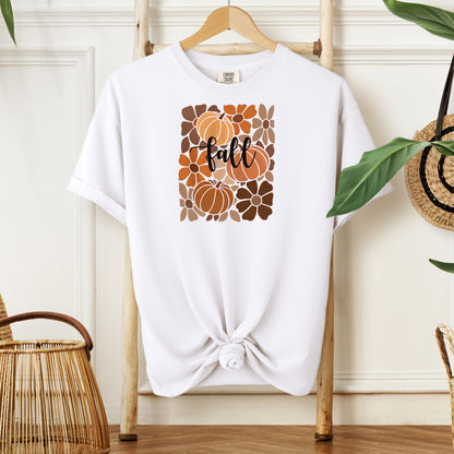 White T-shirt featuring a boho-inspired fall design with hand-drawn pumpkins and flowers in warm autumn tones. The word "fall" is written in elegant script across the center of the graphic, framed by a mosaic-style floral and pumpkin pattern. Perfect for seasonal style and cozy autumn vibes.