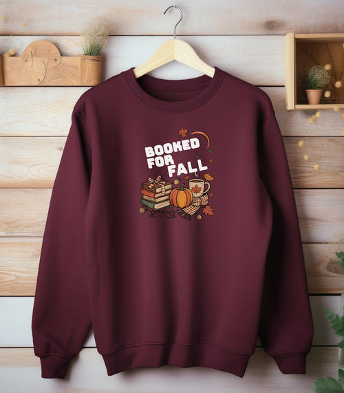 Maroon Gildan sweatshirt featuring a cozy autumn-themed “Booked For Fall” design with stacked books, pumpkin, coffee mug, scarf, glasses, and falling leaves in warm fall tones. Perfect for book lovers who embrace sweater weather, pumpkin spice, and cozy reading sessions during the autumn season.