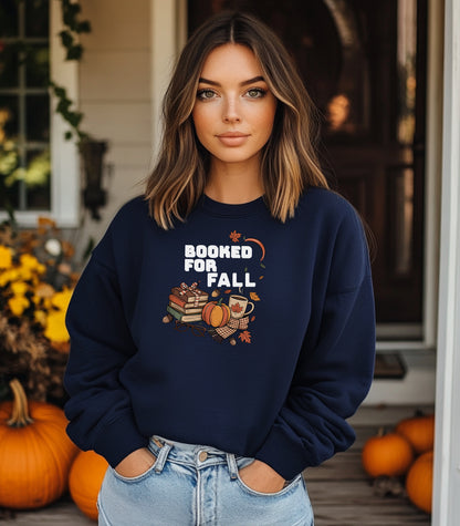 Navy Gildan sweatshirt featuring a cozy autumn-themed “Booked For Fall” design with stacked books, pumpkin, coffee mug, scarf, glasses, and falling leaves in warm fall tones. Perfect for book lovers who embrace sweater weather, pumpkin spice, and cozy reading sessions during the autumn season.