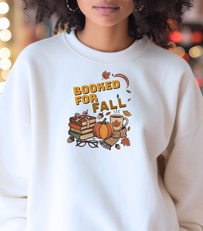 White Gildan sweatshirt featuring a cozy autumn-themed “Booked For Fall” design with stacked books, pumpkin, coffee mug, scarf, glasses, and falling leaves in warm fall tones. Perfect for book lovers who embrace sweater weather, pumpkin spice, and cozy reading sessions during the autumn season.