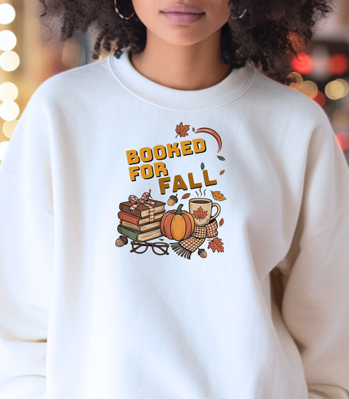 White Gildan sweatshirt featuring a cozy autumn-themed “Booked For Fall” design with stacked books, pumpkin, coffee mug, scarf, glasses, and falling leaves in warm fall tones. Perfect for book lovers who embrace sweater weather, pumpkin spice, and cozy reading sessions during the autumn season.
