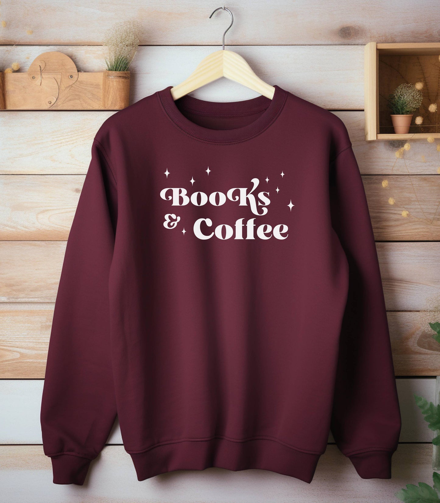 Maroon Gildan sweatshirt featuring a stylish black “Books & Coffee” design in whimsical lettering, accented with small sparkle icons. A cozy and charming look for bookworms and coffee lovers who enjoy slow mornings, warm drinks, and quiet reading time. Perfect for relaxed, literary-inspired outfits.