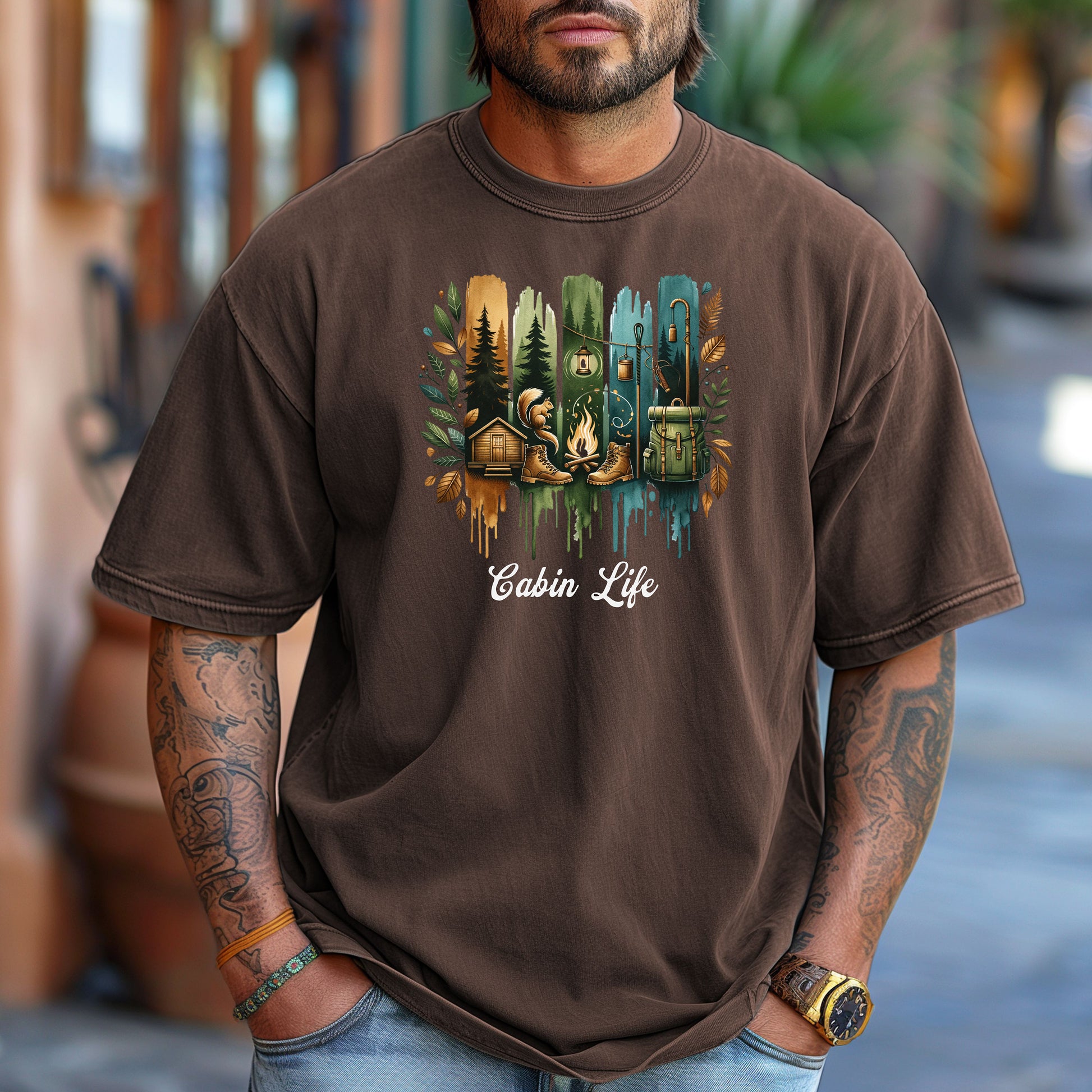 Person wearing an espresso T-shirt with a “Cabin Life” design featuring a colorful, watercolor-style vertical stripe background in earthy tones. The artwork includes pine trees, a log cabin, a campfire with boots, a lantern, and a backpack framed by autumn leaves. A rustic, outdoorsy design perfect for nature lovers, campers, and cabin getaways.