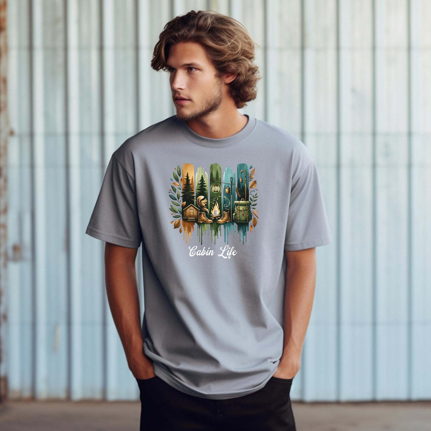 Person wearing a granite T-shirt with a “Cabin Life” design featuring a colorful, watercolor-style vertical stripe background in earthy tones. The artwork includes pine trees, a log cabin, a campfire with boots, a lantern, and a backpack framed by autumn leaves. A rustic, outdoorsy design perfect for nature lovers, campers, and cabin getaways.