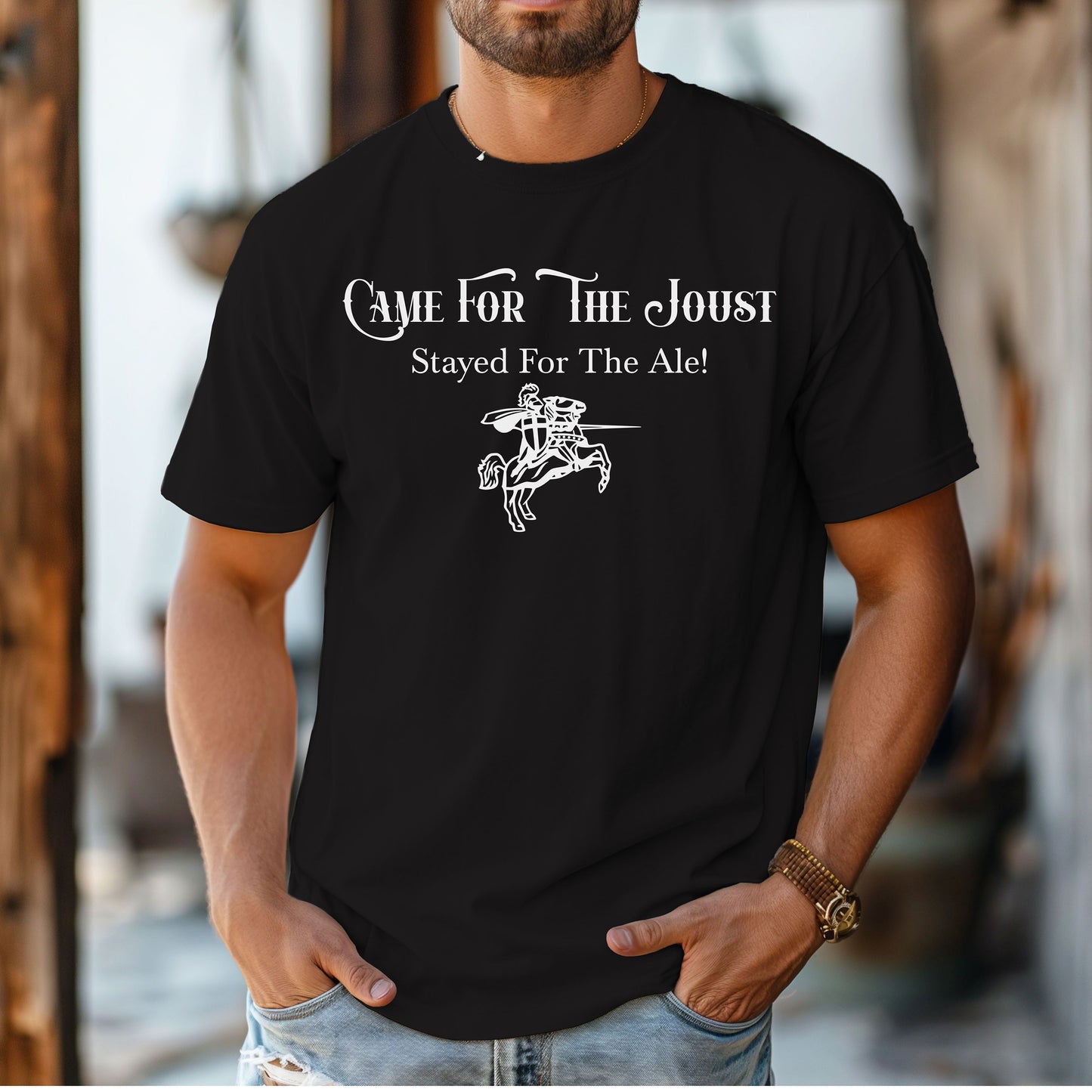 Man wearing a black T-shirt with a fun Renaissance Faire design that reads “Came For The Joust, Stayed For The Ale!” in medieval-style font. The graphic features a white illustration of a jousting knight on horseback with lance raised, capturing the festive spirit of jousting tournaments and hearty faire revelry.