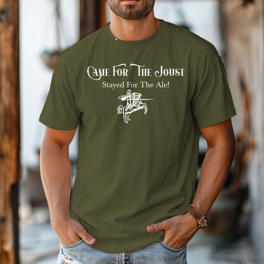 Man wearing a Hemp color T-shirt with a fun Renaissance Faire design that reads “Came For The Joust, Stayed For The Ale!” in medieval-style font. The graphic features a white illustration of a jousting knight on horseback with lance raised, capturing the festive spirit of jousting tournaments and hearty faire revelry.