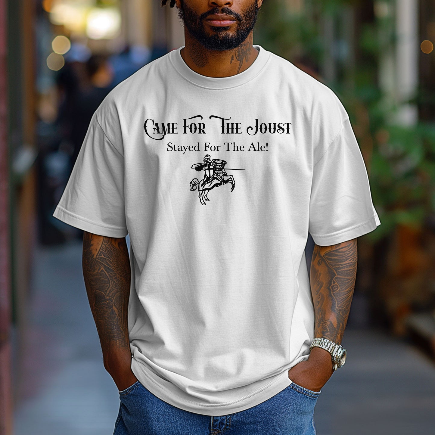 Man wearing a White T-shirt with a fun Renaissance Faire design that reads “Came For The Joust, Stayed For The Ale!” in medieval-style font. The graphic features a white illustration of a jousting knight on horseback with lance raised, capturing the festive spirit of jousting tournaments and hearty faire revelry.
