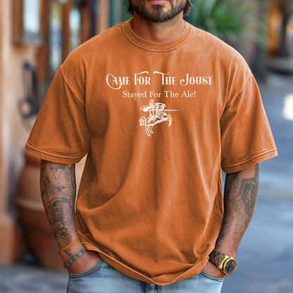 Man wearing a Yam T-shirt with a fun Renaissance Faire design that reads “Came For The Joust, Stayed For The Ale!” in medieval-style font. The graphic features a white illustration of a jousting knight on horseback with lance raised, capturing the festive spirit of jousting tournaments and hearty faire revelry.