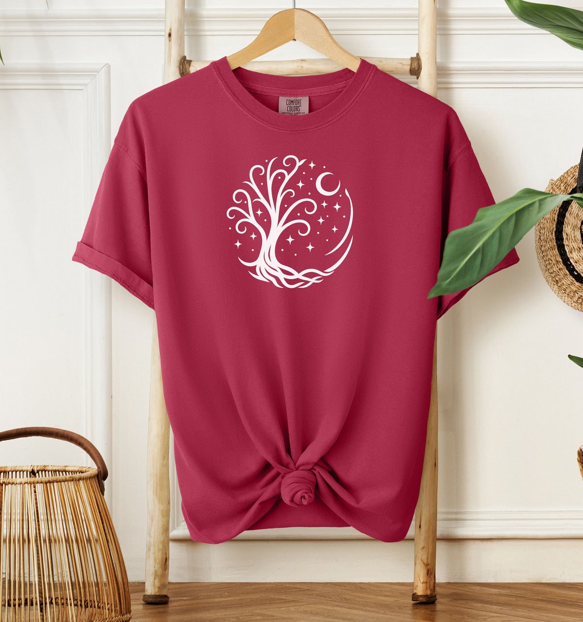 Celestial Tree of Life T-shirt featuring a white mystical tree design within a circular frame of stars, crescent moon, and swirling roots. Printed on a chili red unisex Comfort Colors tee, this nature-inspired celestial design is perfect for free spirits, stargazers, boho style lovers, and anyone drawn to cosmic, spiritual, or magical themes.