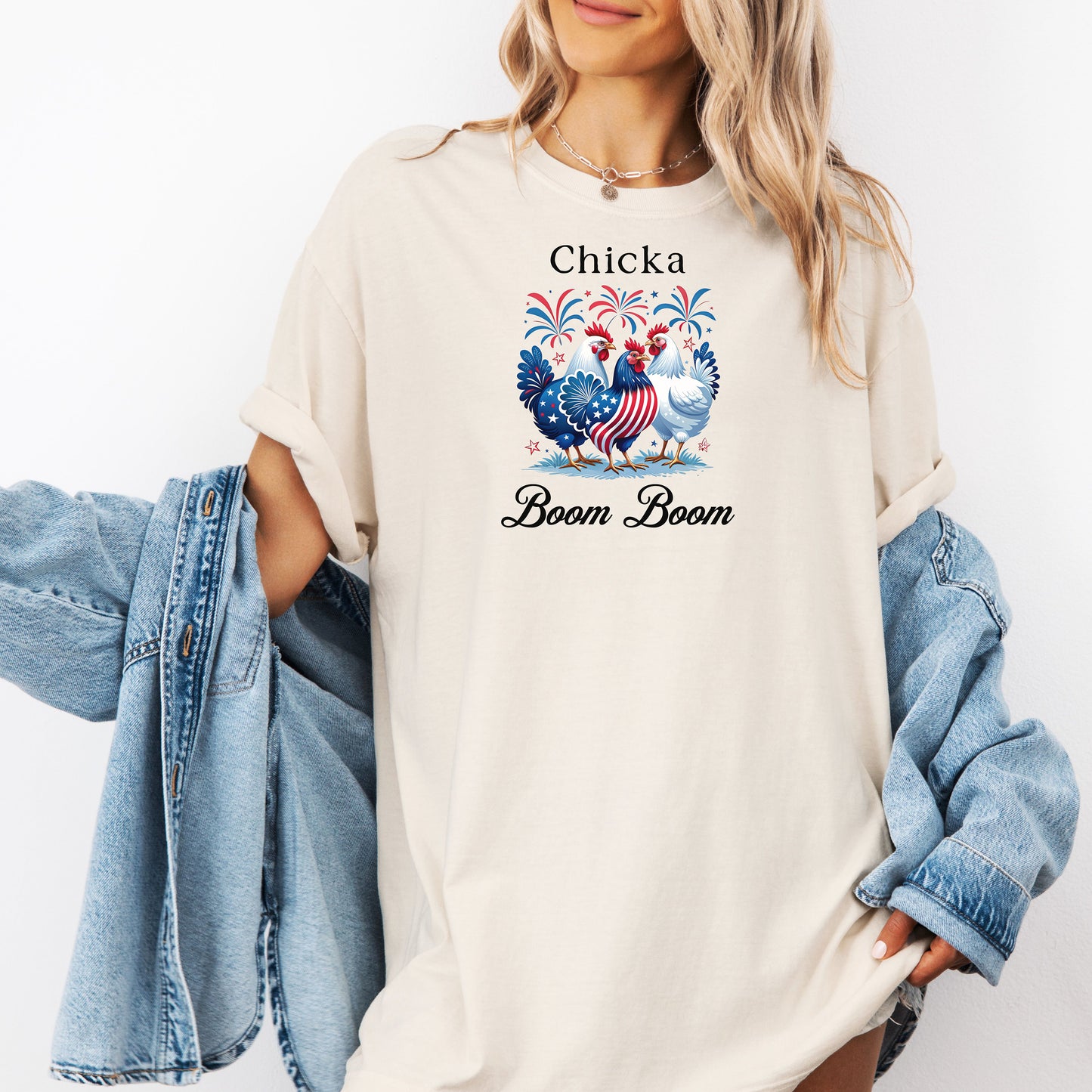 Ivory t-shirt featuring a playful 'Chicka Boom Boom' design with three patriotic chickens, one decorated in red, white, and blue stars and stripes, and the other in white, surrounded by colorful fireworks. A third chicken is decorated in red and white stars on a blue body.  A fun and festive shirt perfect for 4th of July, barbecues, summer parties, and casual patriotic celebrations.