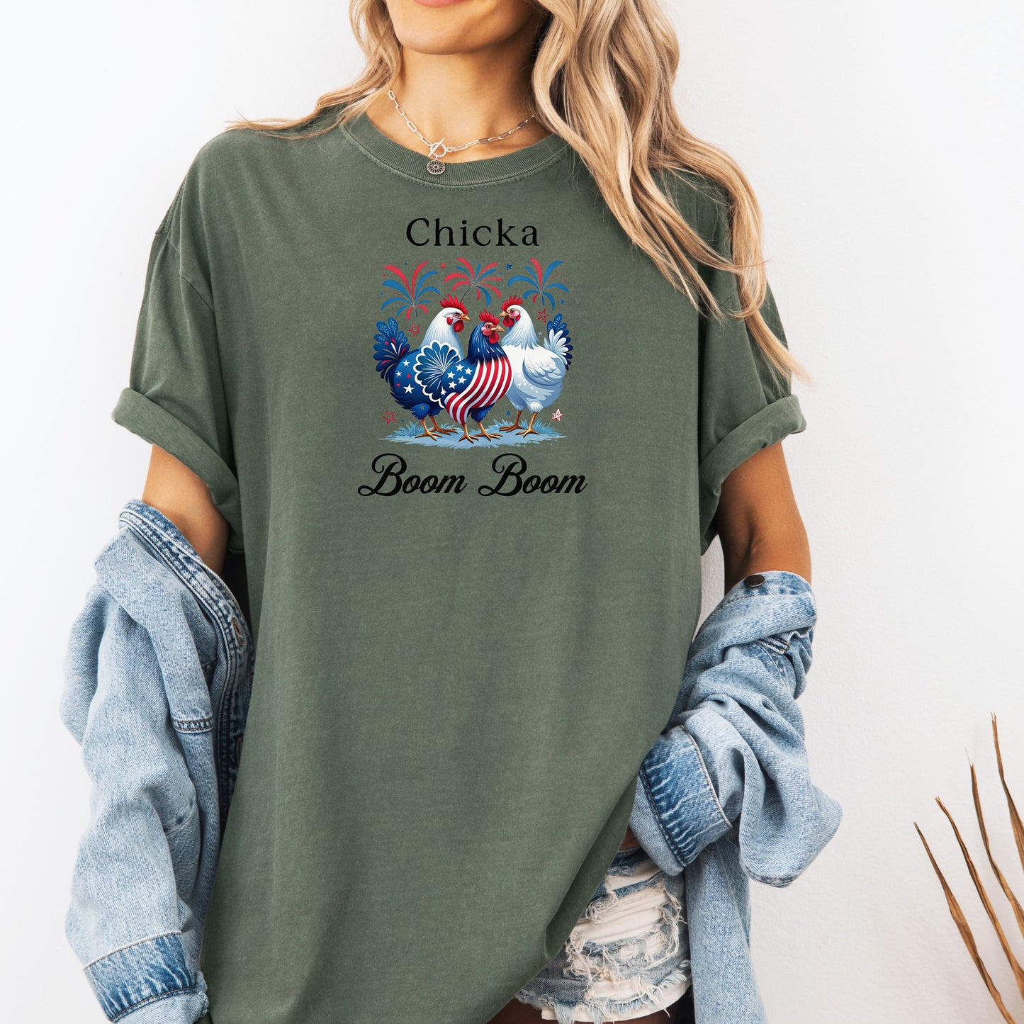 Moss t-shirt featuring a playful 'Chicka Boom Boom' design with three patriotic chickens, one decorated in red, white, and blue stars and stripes, and the other in white, surrounded by colorful fireworks. A third chicken is decorated in red and white stars on a blue body.  A fun and festive shirt perfect for 4th of July, barbecues, summer parties, and casual patriotic celebrations.