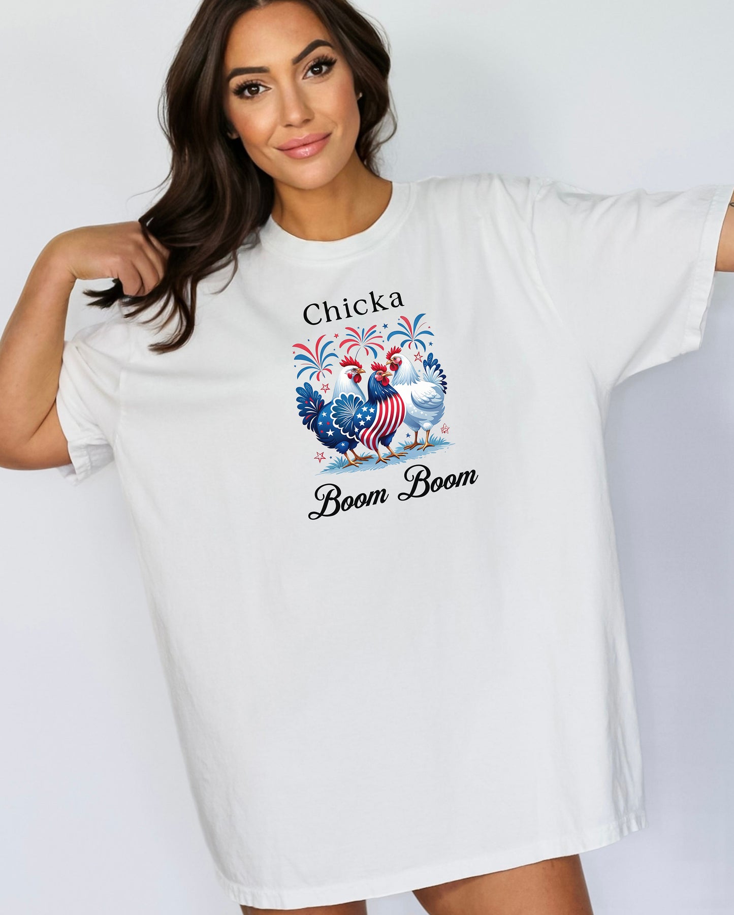 White t-shirt featuring a playful 'Chicka Boom Boom' design with three patriotic chickens, one decorated in red, white, and blue stars and stripes, and the other in white, surrounded by colorful fireworks. A third chicken is decorated in red and white stars on a blue body.  A fun and festive shirt perfect for 4th of July, barbecues, summer parties, and casual patriotic celebrations.
